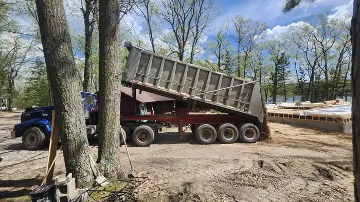 Blue tri-axle dump trailer tipping a load of fill