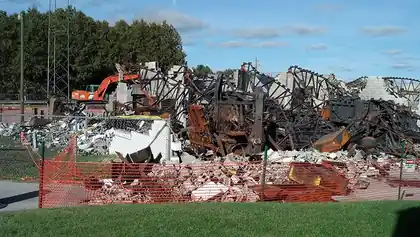 Burned building coming down, charred framing and debris on the ground
