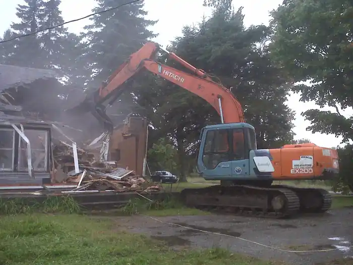 Excavator pulling down a two-storey house into a debris pile