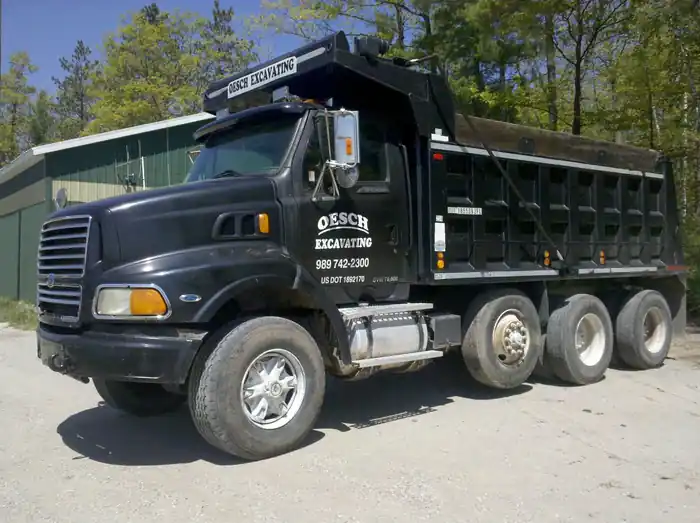 Black tri-axle dump truck lettered Oesch Excavating on the door