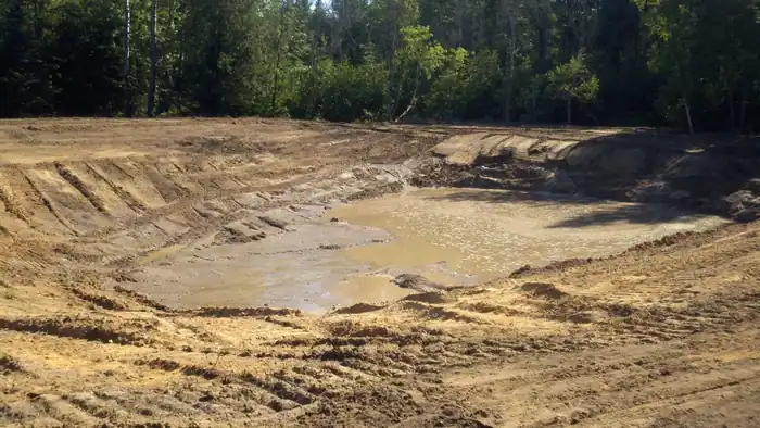 Freshly dug pond basin in sand with water collecting in the bottom