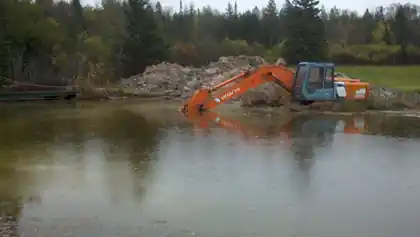 Orange Hitachi excavator standing in the pond it is digging, reflected in the water