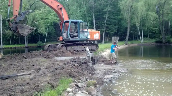 Orange Hitachi excavator shaping the shoreline of a new pond