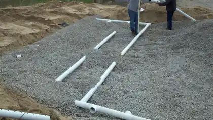 White PVC distribution pipe set into a sloped bed of crushed gray gravel beside sand cuts